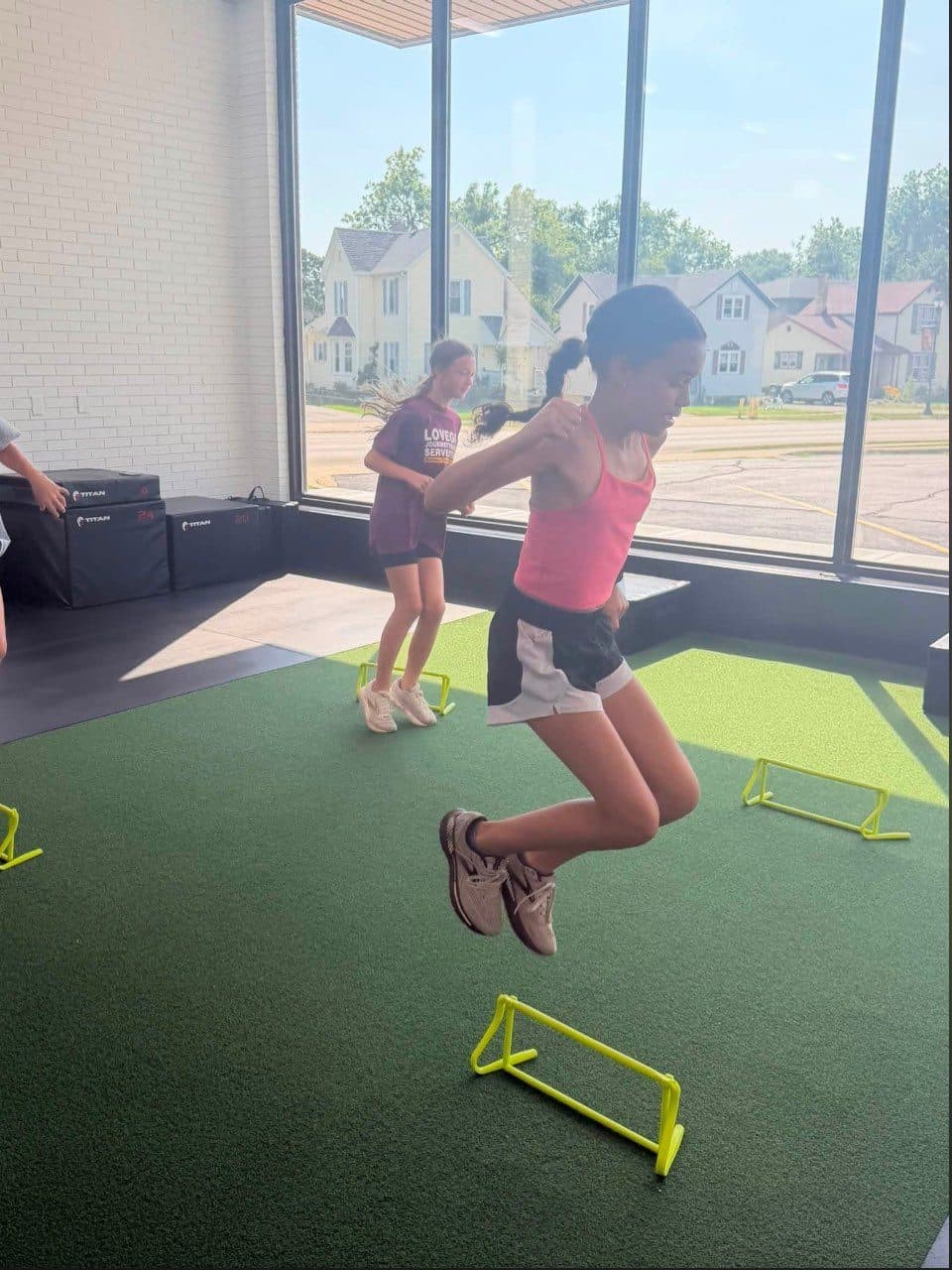 Young athlete mid-hop over a mini hurdle on the turf