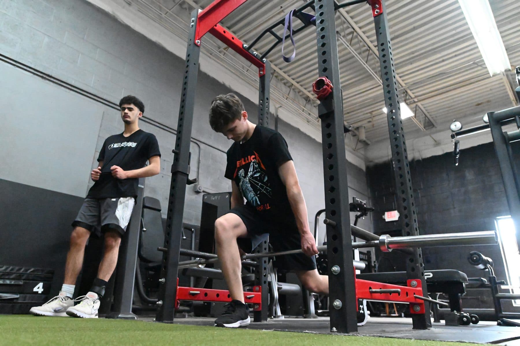 Athlete in the bottom of a split squat inside the rack, straddling a barbell, coach watching