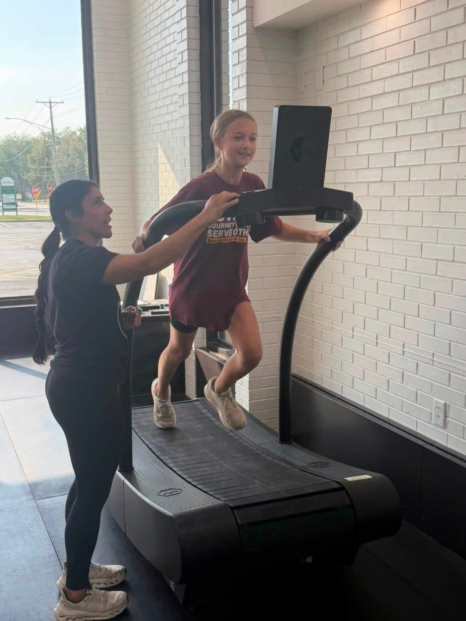 Athlete sprinting on a curved treadmill while a Batti coach stands beside her