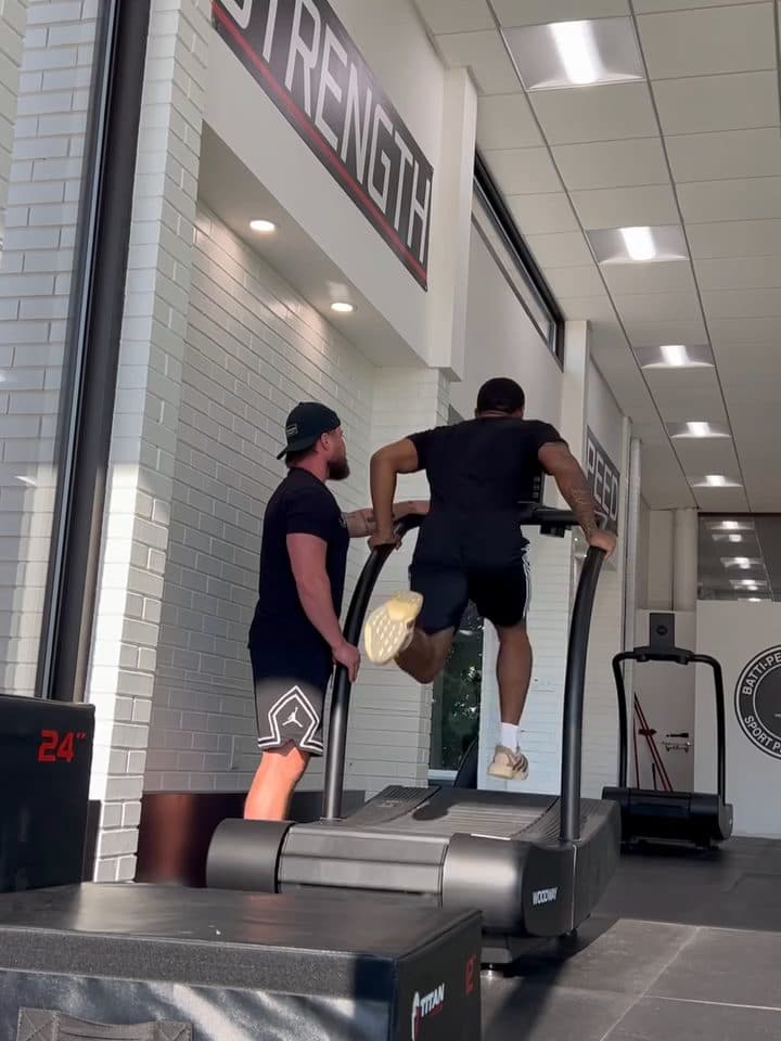 Athlete sprinting on a curved treadmill while a coach watches at the rail