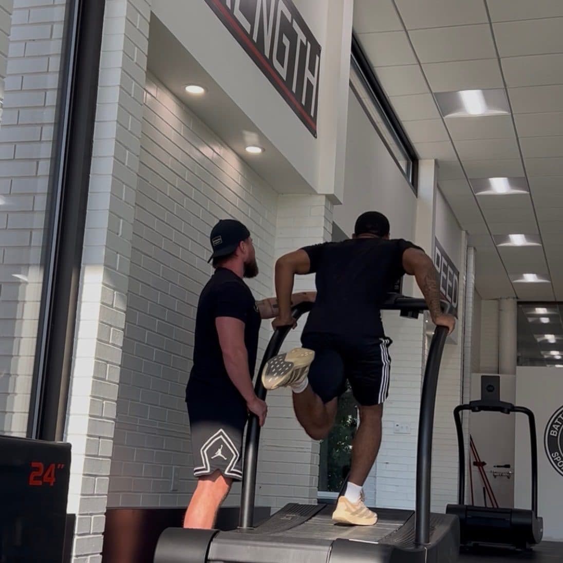Athlete sprinting on a curved treadmill with a high knee drive while a coach spots at the rail