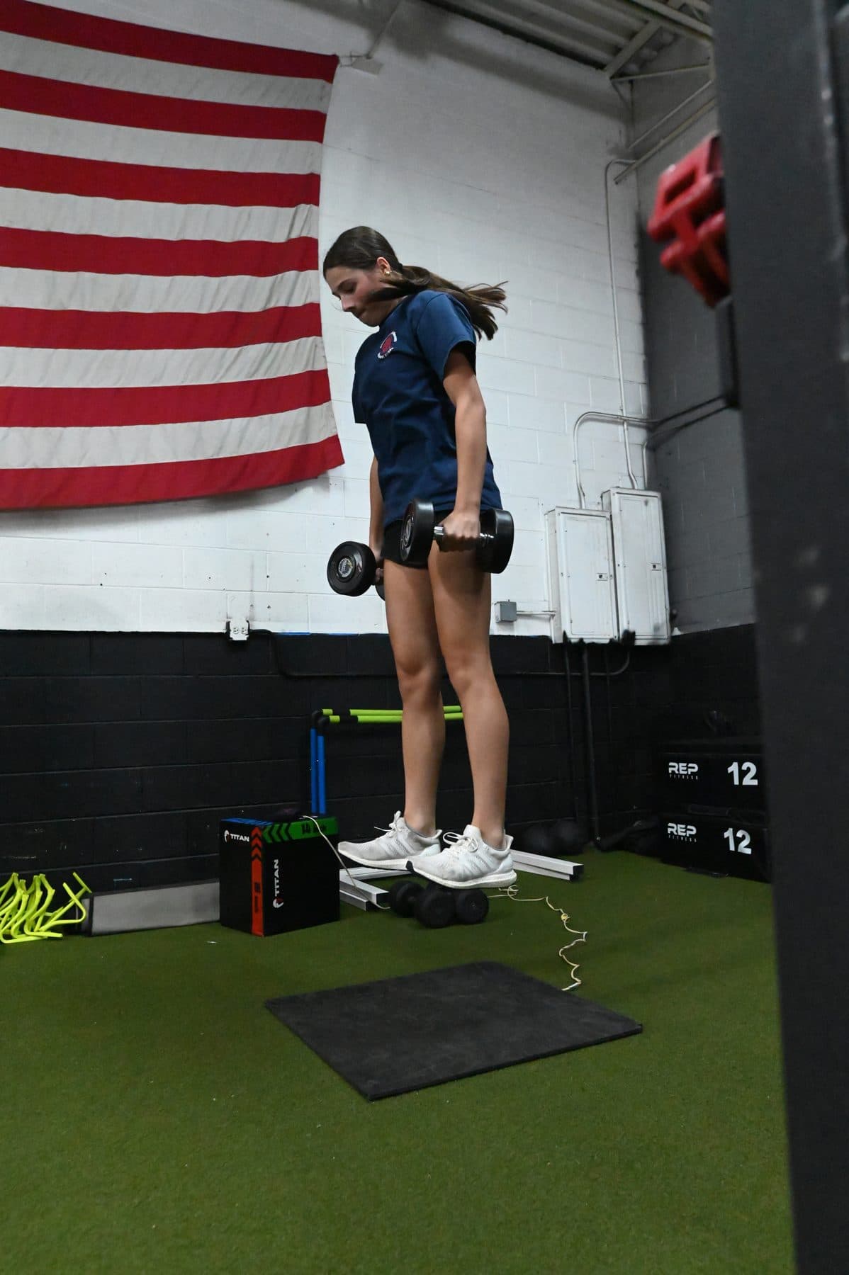 Athlete airborne in a dumbbell-loaded vertical jump over the jump mat
