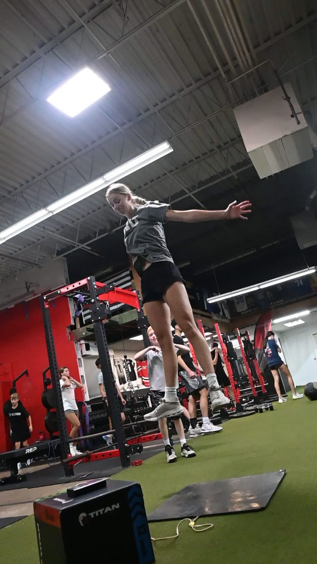 Athlete at the peak of an approach jump, one arm reaching high over the jump mat