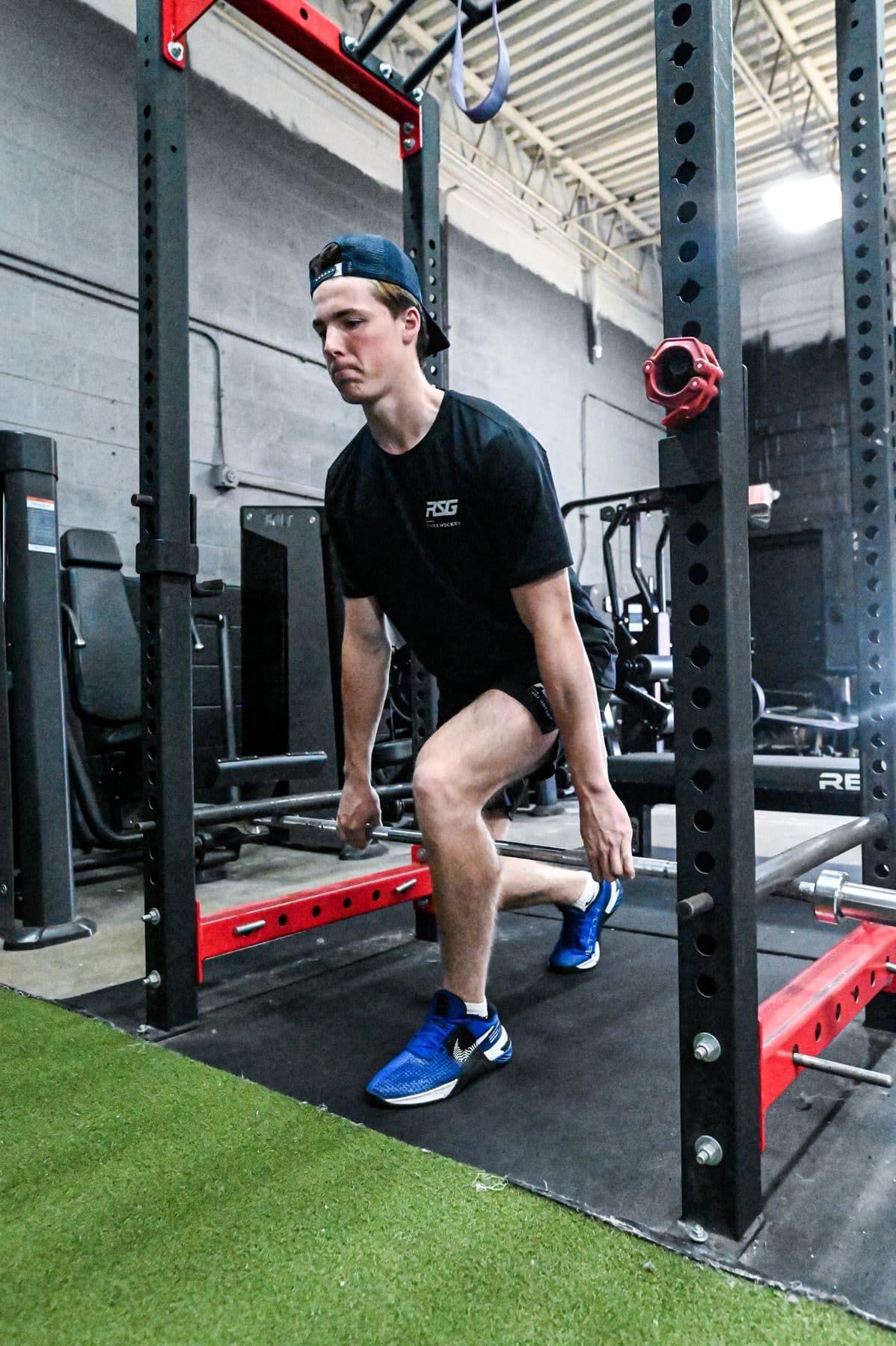 Athlete in a split stance gripping a barbell inside the rack