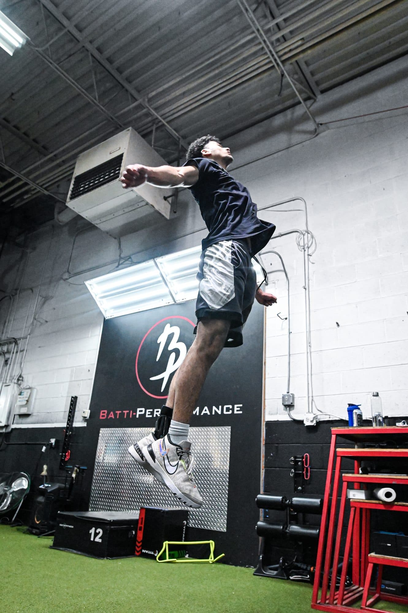 Batti athlete in the air during a vertical jump in front of the Batti Performance logo wall